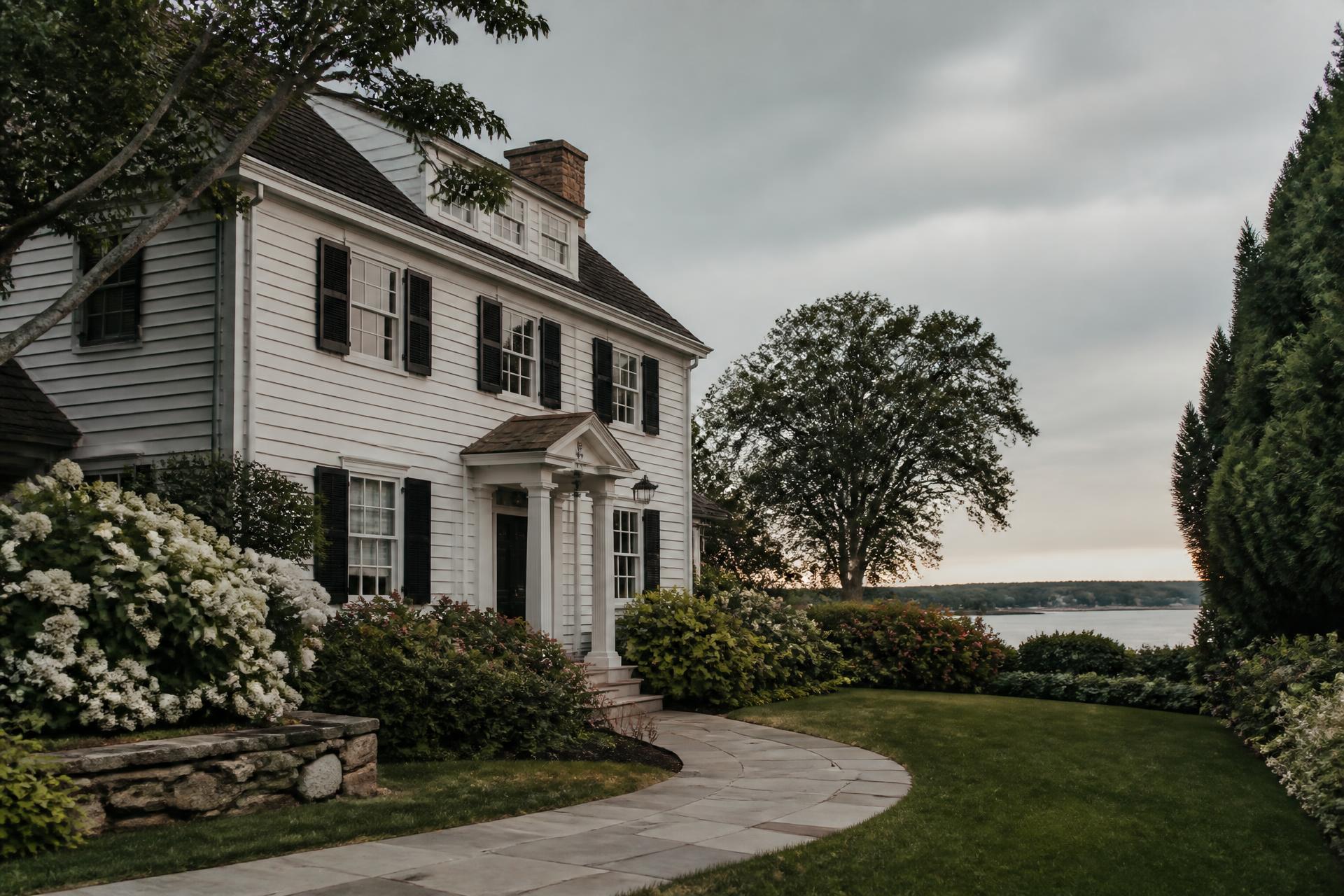 A white clapboard colonial home with black shutters and mature landscaping on a Fairfield County property